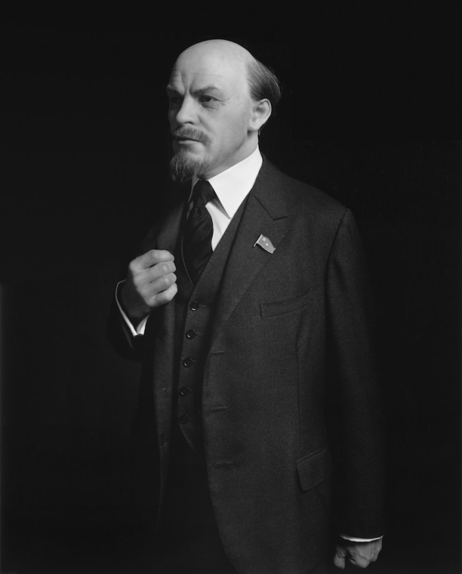 Black-and-white three quarter portrait of a wax figure of a man in a suit jacket and tie with one closed hand over his chest
