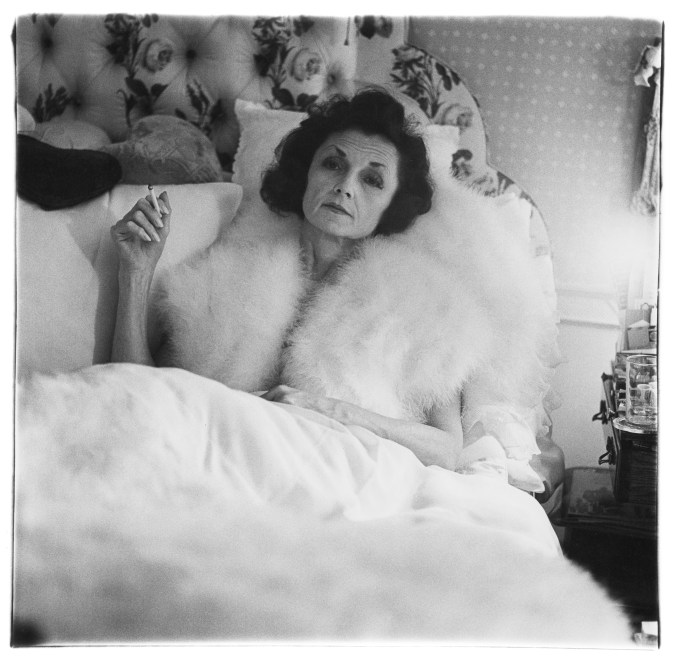 Black and white photograph of a figure in a fuzzy shawl with a cigarette in bed