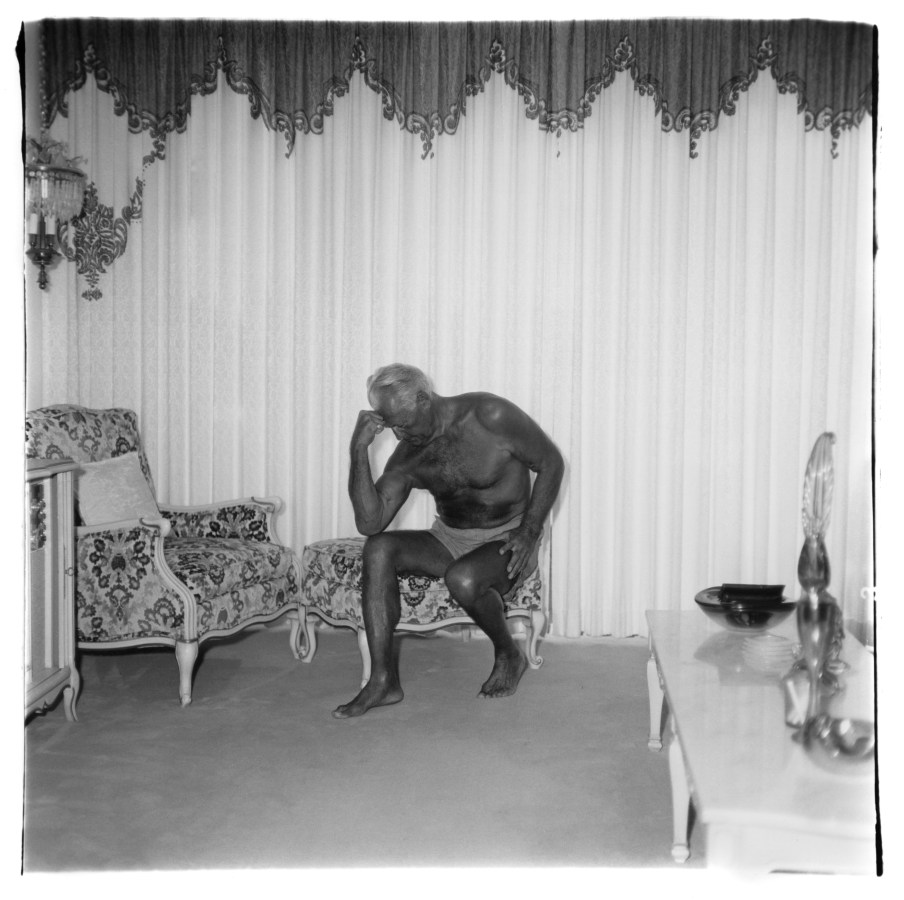 Black-and-white photograph of a tanned man sitting with his head resting on his hand
