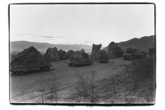A black and white image of a mountain landscape with a dirt road and large boulder-like rocks on dollies