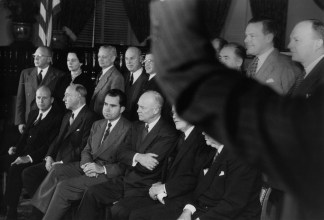 Black-and-white group portrait of politicians in two rows with raised arm in the foreground