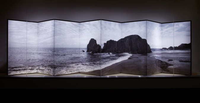 Color image of a folding screen with an image of a shore with large rock formations mounted onto the screen