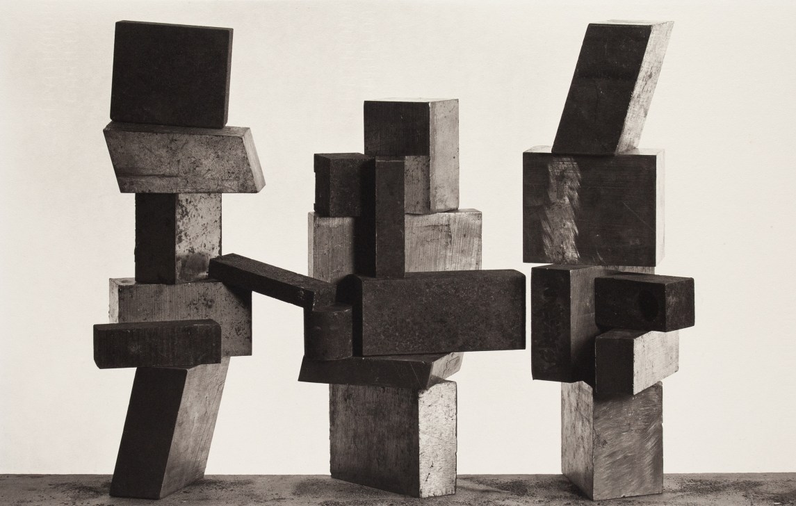 Black and white photograph of three sculptures made of wooden blocks against a white wall