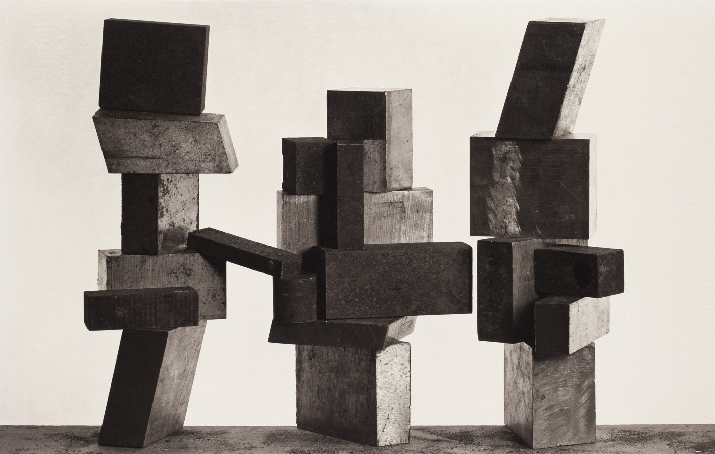 Black and white photograph of three sculptures made of wooden blocks against a white wall