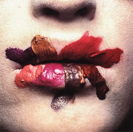 Color photograph of a mouth up close smeared with varying shades of red lipstick