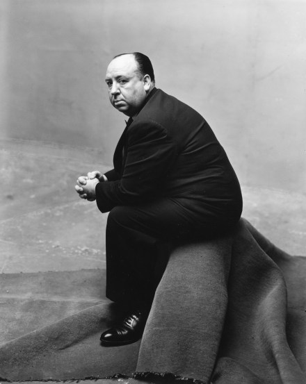 Black and white photograph of a portly man seated on a rug-covered stool
