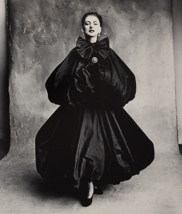 Black and white photograph of a figure in a bouncy, structured black dress in a studio
