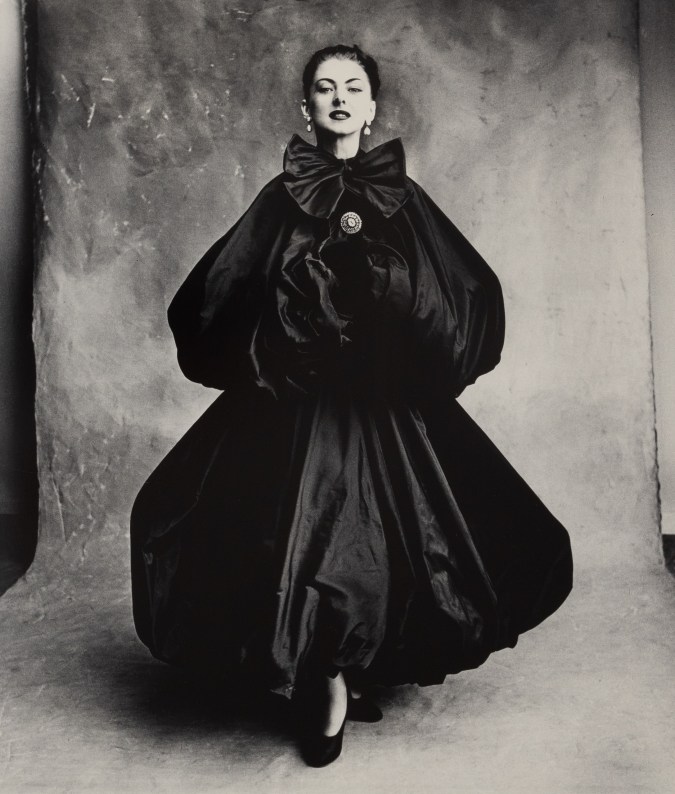 Black and white photograph of a figure in a bouncy, structured black dress in a studio