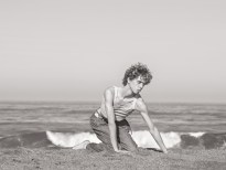 Black and white photograph of a figure on the beach on their hands and knees
