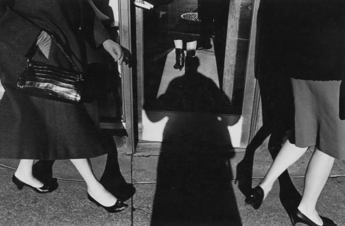Black and white photograph depicting a silhouetted shadow with three pairs of legs walking