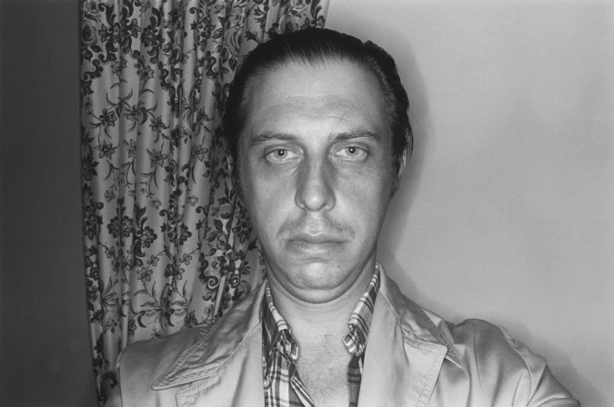 A black and white photograph of the artist taken with flash against a wall.