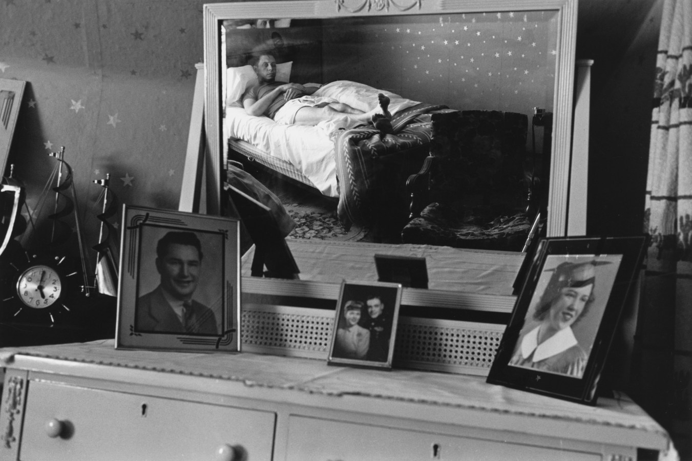 Black and white photograph of figure laying in a bed reflected through a mirror
