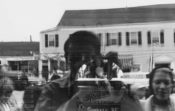 A black and white photograph of the artists reflection in a window.
