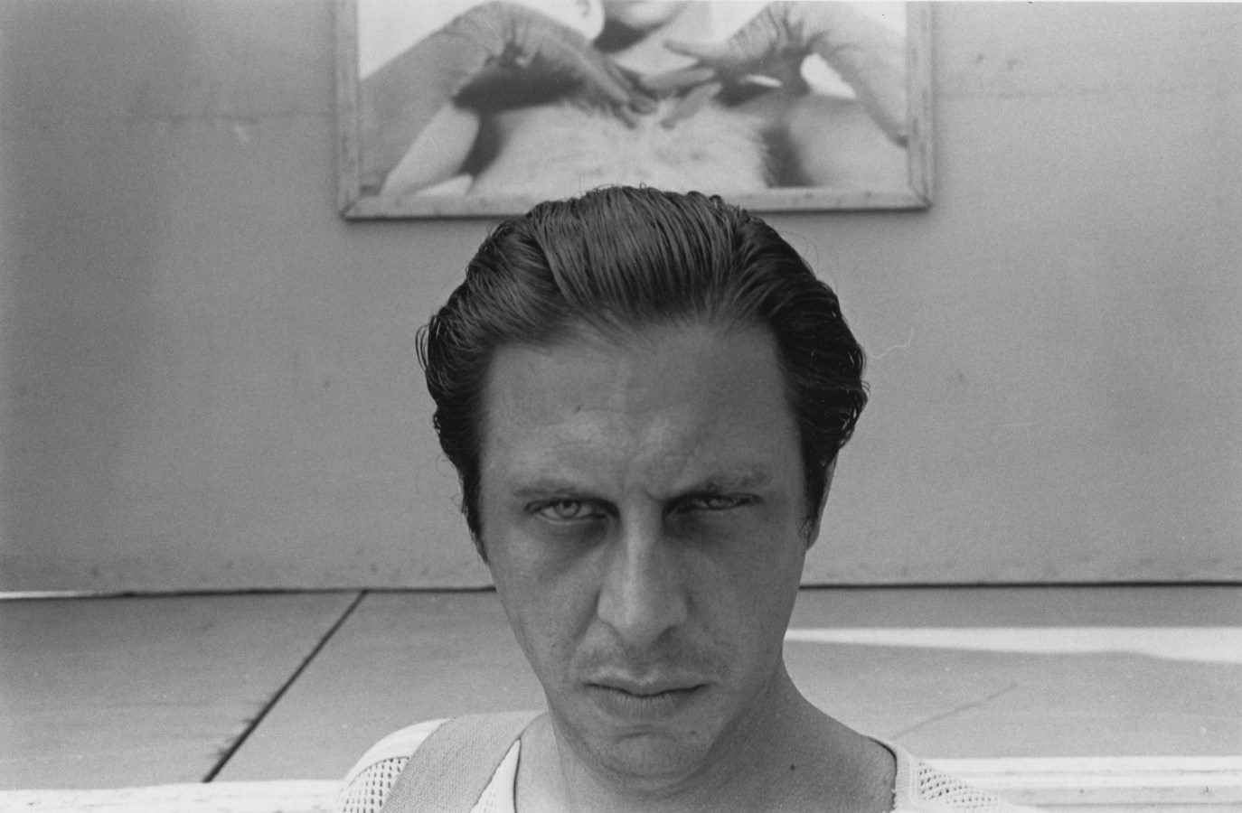 A black and white portrait of the artist in front of an advertisement depicting a woman's arms.