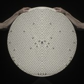 Color image of two hands holding a wheel with pegs and a white ball against a black background