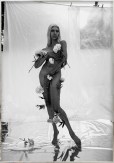 Color image of a black and white photograph of a nude figure covered with flowers and covering their body with their hands framed in distressed metal