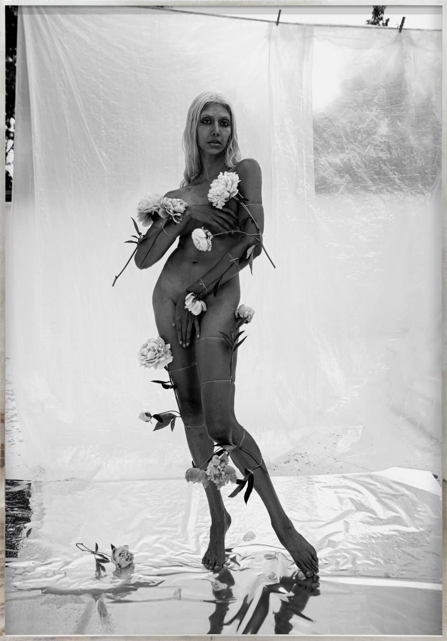 Color image of a black and white photograph of a nude figure covered with flowers and covering their body with their hands framed in distressed metal