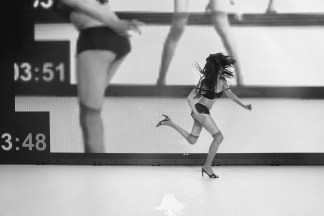 A black and white photograph features a woman in heels jumping across a stage