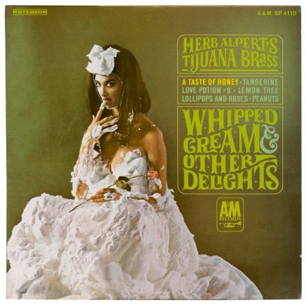 A collage consisting of a vinyl record by Herb Alpert's Tijuana Brass band and mixed media shows a woman covered in whipped cream licking her tongue