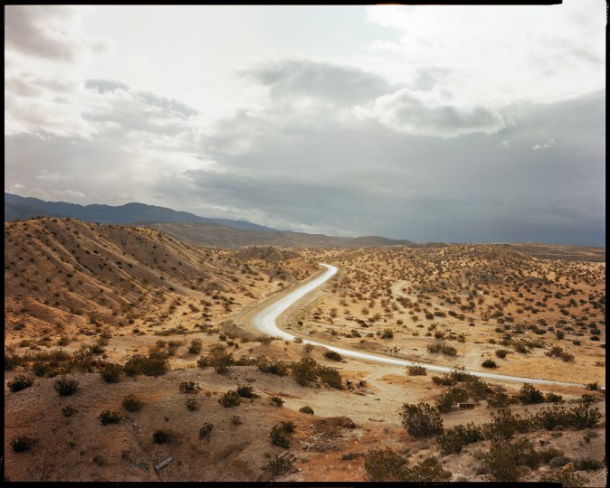 Color photograph of a desert road with debris throughout