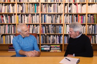 Two men conversing at a table in front of a wall of books
