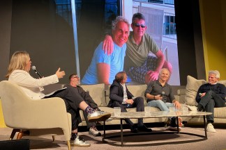 An image of five people seated in conversation on stage in front of a projected screen
