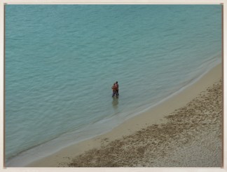 A framed color photograph depicting two people in the distance, hugging on the beach while staring out to sea