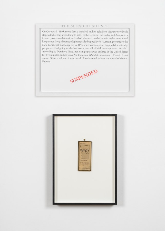 Color image of an artwork including a text panel and a framed newspaper graphic against a white wall