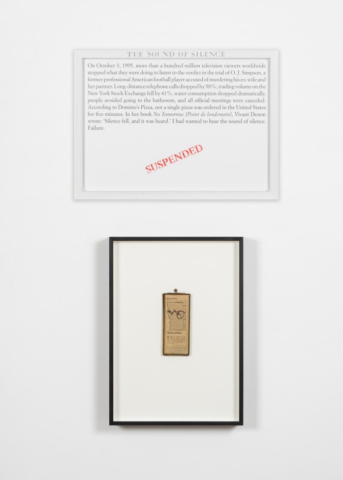 Color image of an artwork including a text panel and a framed newspaper graphic against a white wall
