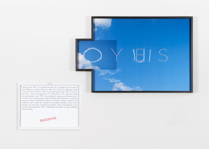 Color image of an artwork including a text panel and a color photograph of the sky that has the word 'oui' written out in the sky