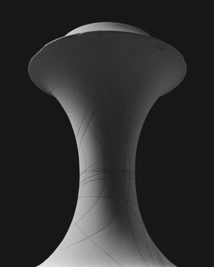 A black and white photograph of an hourglass shaped sculpture, starkly lit