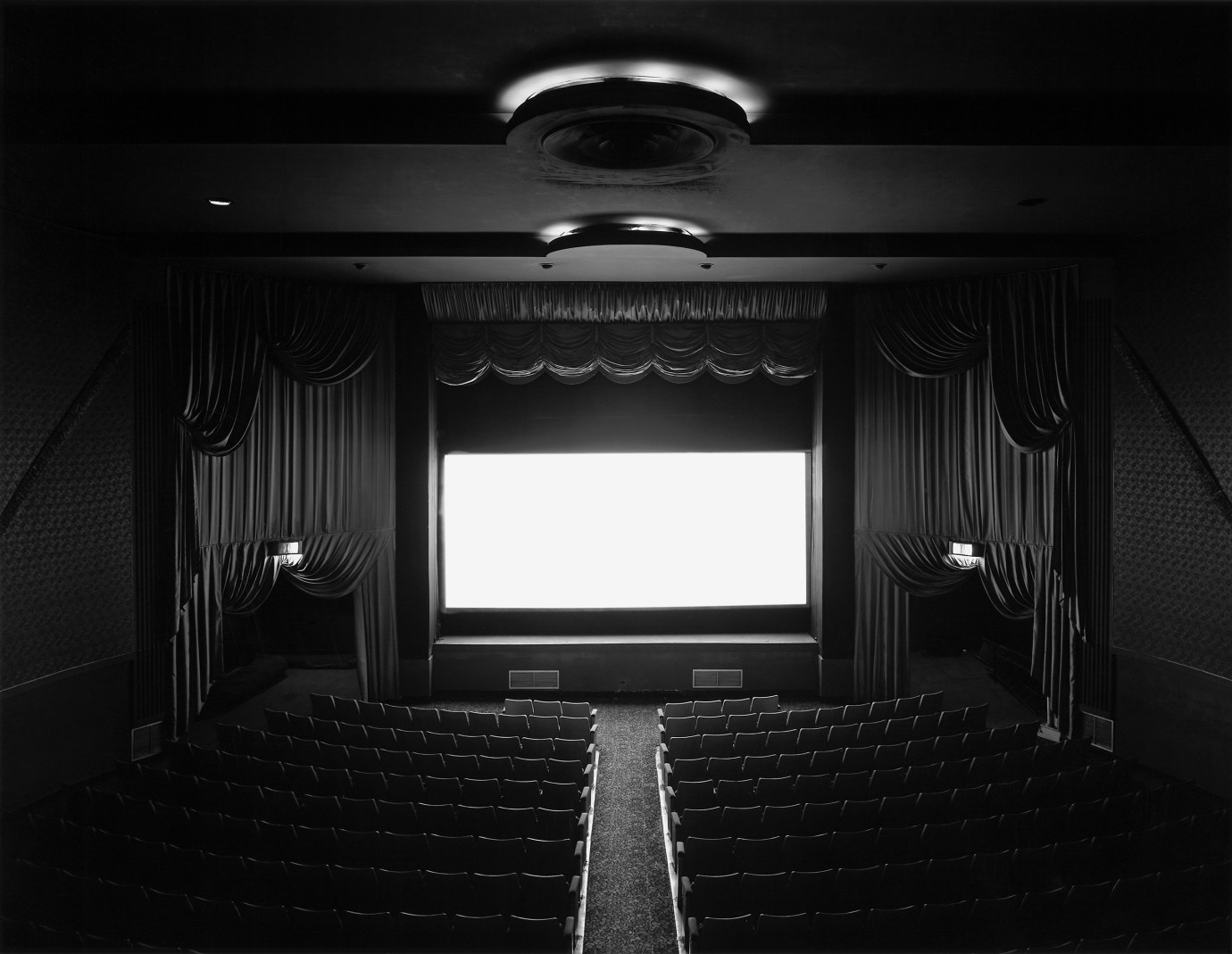 Black and white photograph of the interior of a movie theater with light emanating from the screen