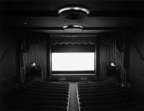 Black and white photograph of the interior of a movie theater with light emanating from the screen