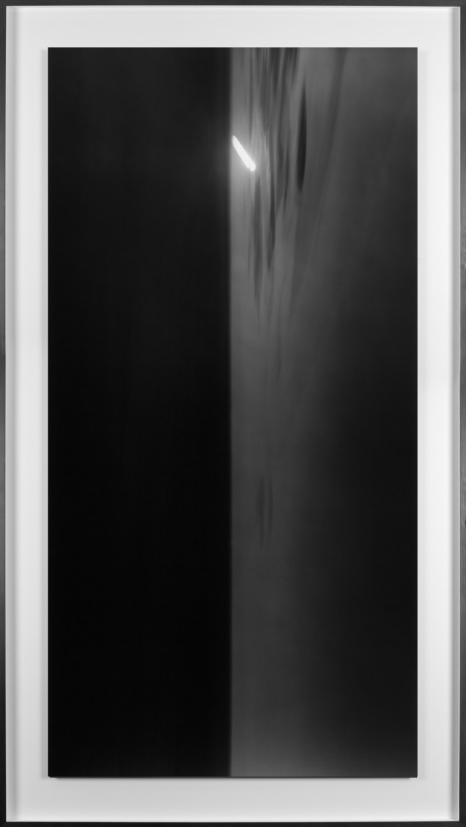 Black and white photograph of the ocean horizon at night with a long exposure of the moon framed in black