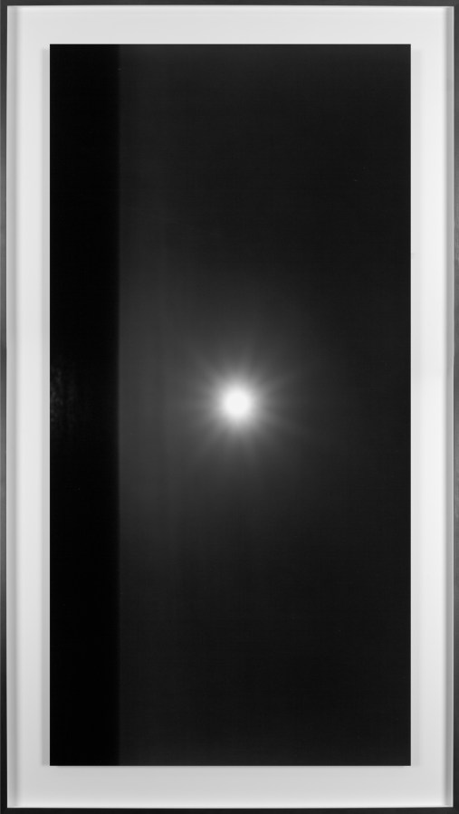 Black and white photograph of the ocean horizon with the moon above the horizon line framed in black