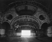 Black-and-white photograph of an empty abandoned theater with a glowing blank white screen