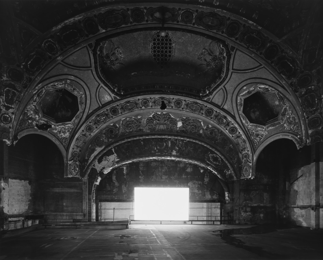 Black-and-white photograph of an empty abandoned theater with a glowing blank white screen