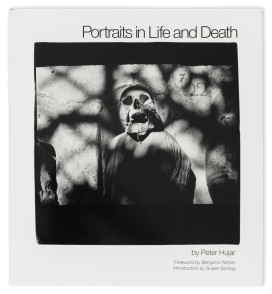 Photograph of a white hardcover book with an black-and-white image of a skull and body, surrounded by a rock edifice, printed on it